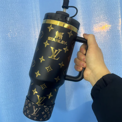 Hand holding a Stanley tumbler with Louis Vuitton pattern against a blue background