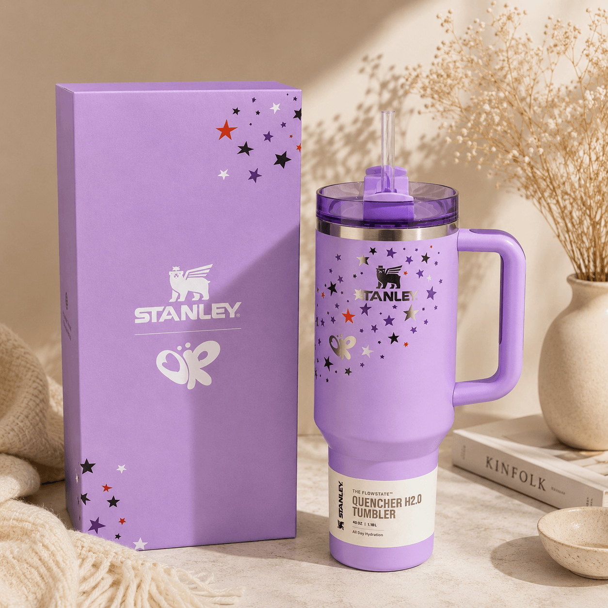Purple Stanley tumbler with handle and stars on a beige surface with packaging and decor items.