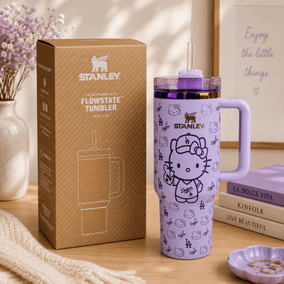 Purple Stanley tumbler with Hello Kitty design next to its packaging on a wooden surface.