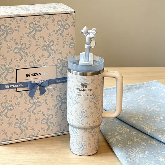 Stanley tumbler with decorative elements next to a branded box on a wooden surface.
