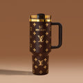 Stanley 40oz insulated tumbler featuring luxury-inspired brown monogram pattern, gold accents, black ergonomic handle, and premium insulated design